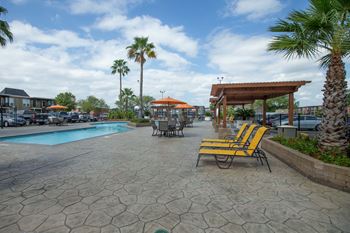 A pool area with a patio, chairs and umbrellas at Willow Creek Apartments, Houston, TX, 77012